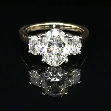 Three-stone ring with an oval center diamond and oval side diamonds on a yellow gold band