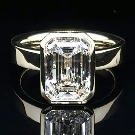 Emerald-cut diamond in a bezel setting on a wide yellow gold band