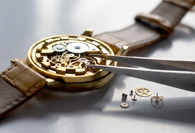 Tweezers adjusting the movement of a gold watch during a repair