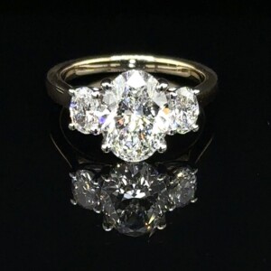 Three-stone ring with an oval center diamond and oval side diamonds on a yellow gold band