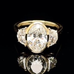 Bezel-set oval diamond with half-moon side diamonds on a yellow gold band